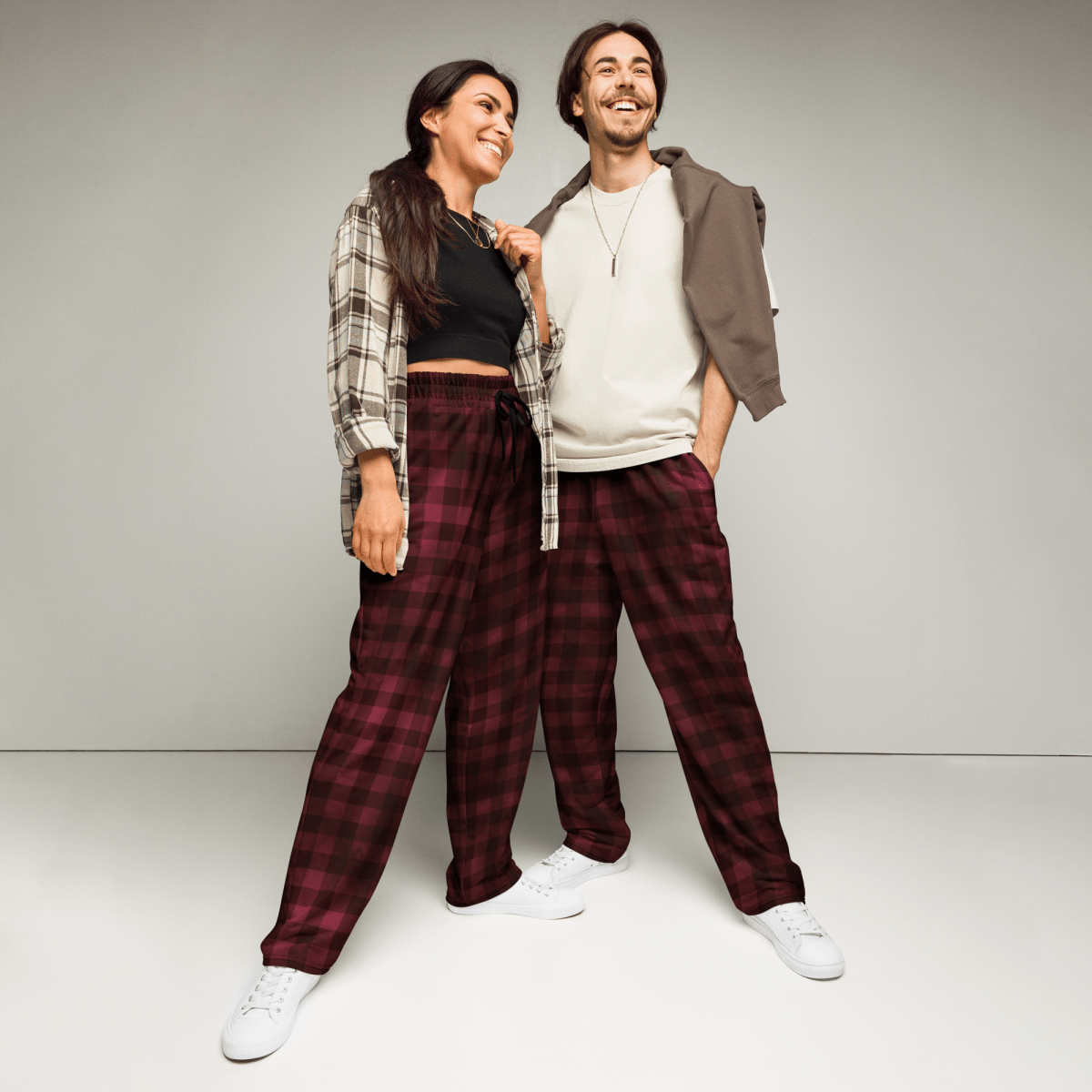 Two people wearing matching plaid pants and casual tops against a plain background