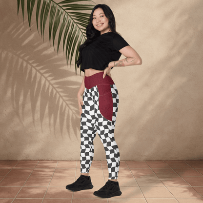 Woman wearing a black crop top and checkered pants with a burgundy waistband, standing against a beige wall.
