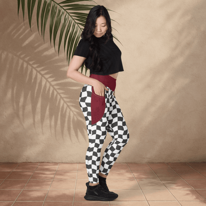 Woman wearing a black top and burgundy with checkered print leggings against a beige wall.
