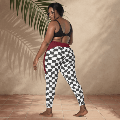 Woman wearing checkered pants and a black top against a beige wall with a plant.