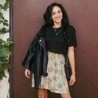 Woman wearing a black jacket, black top, and floral skirt against a brown wall.