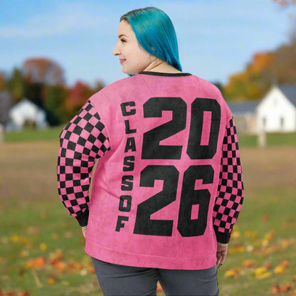 Person wearing a pink sweatshirt with 'Class of 2026' text and checkered sleeves outdoors