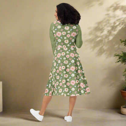 Woman wearing a green floral dress against a beige wall.