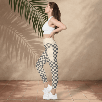 Woman wearing a white sports bra and checkered leggings standing against a beige wall with a palm leaf.