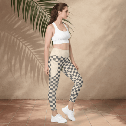 Woman wearing a white sports bra and checkered leggings standing against a beige wall with a palm leaf.
