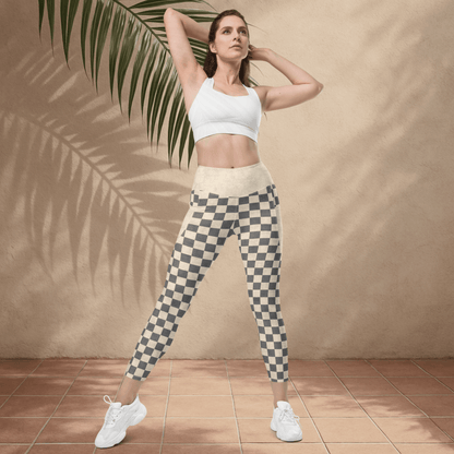 Woman wearing a white sports bra and checkered leggings standing against a beige wall with a palm leaf.