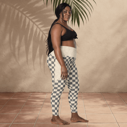 Woman wearing a black top and checkered pants standing against a beige wall with a plant.