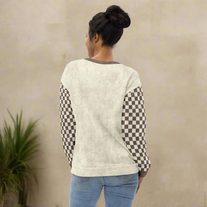 Person wearing a cream sweater with checkered sleeves on a neutral background