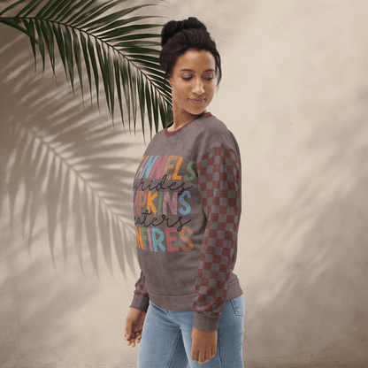 Woman wearing an espresso and burgundy sweater with colorful text design, standing against a beige wall with a palm leaf.
