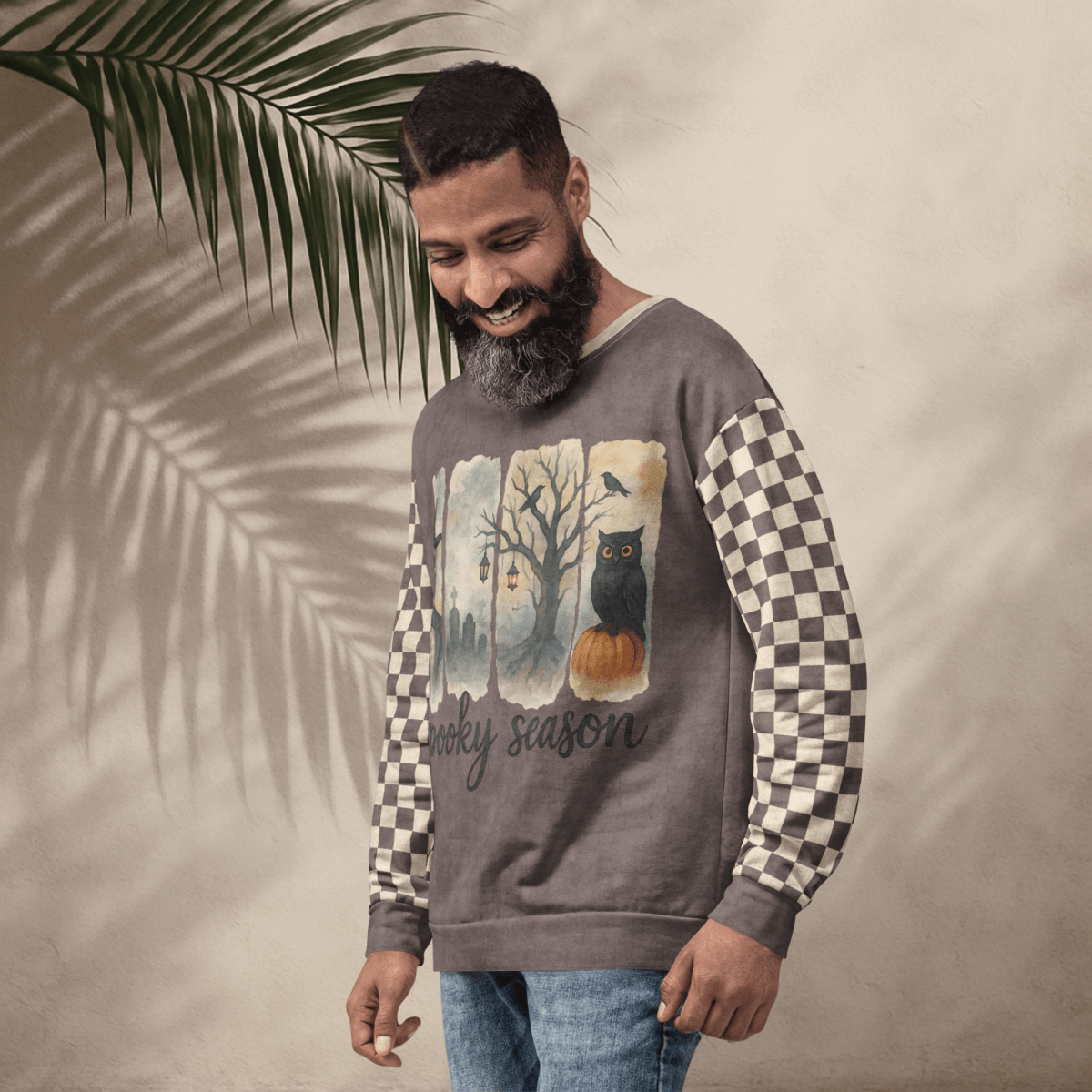 Man wearing a sweater with a checkered pattern and Spooky Season Halloween Design, standing against a neutral background with a leaf.