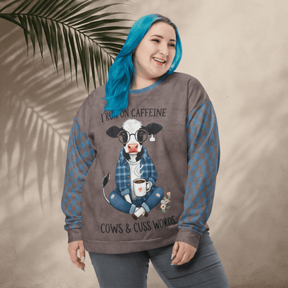 Person wearing Espresso and denim Sweatshirt with a cow graphic and text, standing against a beige wall with a leafy branch.