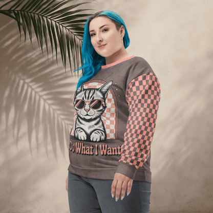 model wearing Espresso sweatshirt with a sunglasses-wearing tabby cat and “I Do What I Want” text; sleeves feature pink-and-espresso checkerboard pattern with pink collar and cuffs.