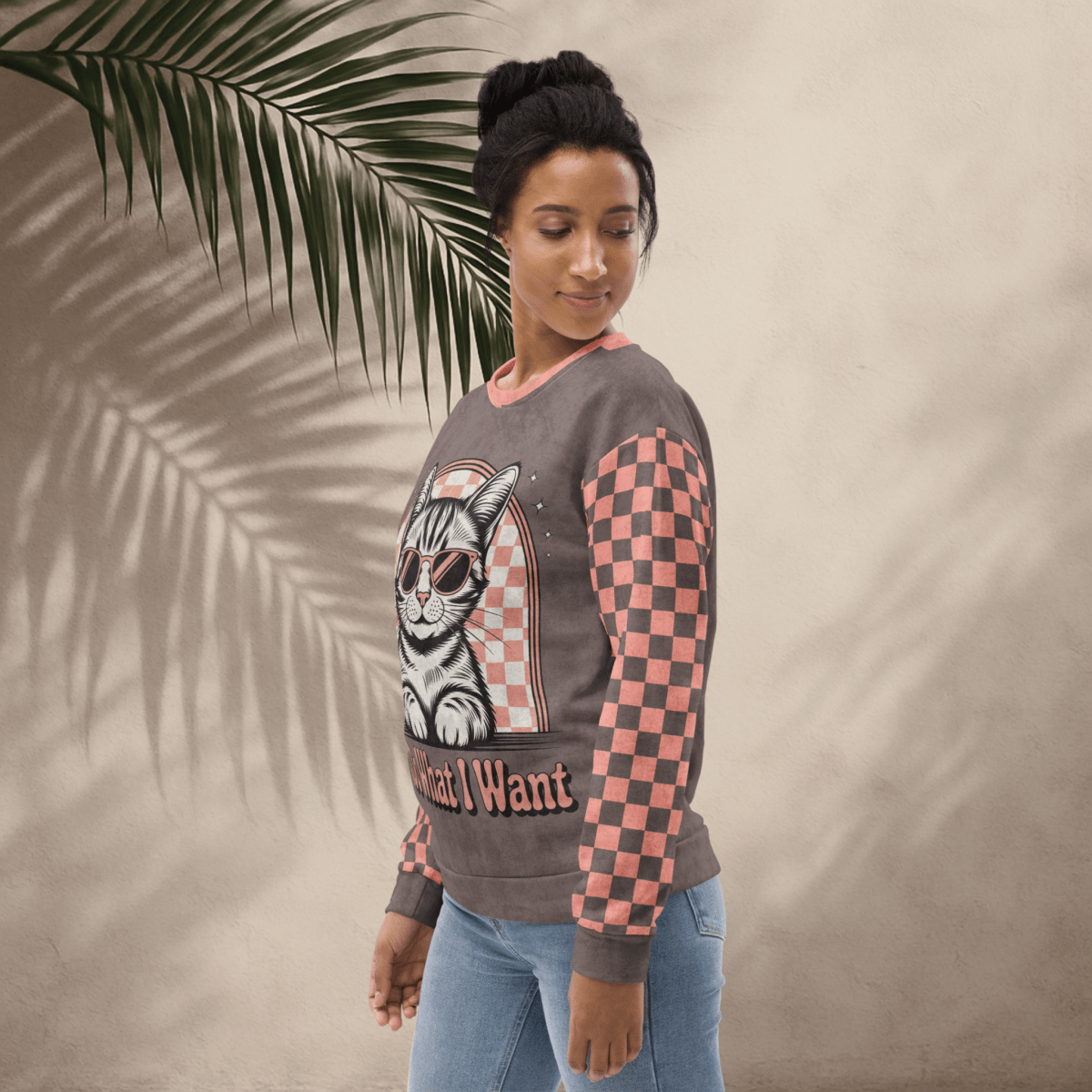 model wearing Espresso sweatshirt with a sunglasses-wearing tabby cat and “I Do What I Want” text; sleeves feature pink-and-espresso checkerboard pattern with pink collar and cuffs.