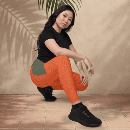 Woman wearing orange patterned leggings and black shoes sitting on a tiled floor with a beige wall and plant in the background.