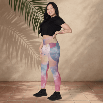 Woman wearing colorful leggings and a black crop top standing against a beige wall with a leafy branch.