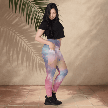 Woman wearing colorful leggings and a black top against a beige wall with a leafy branch.