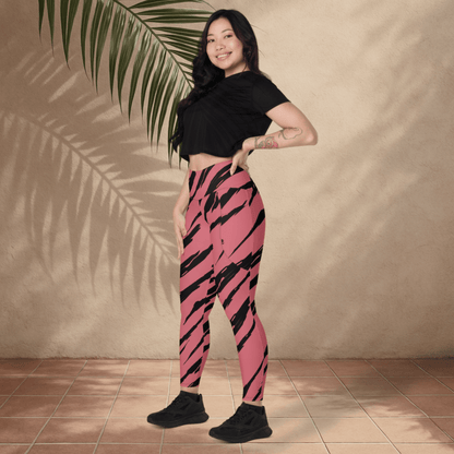 Woman wearing pink and black striped leggings standing against a beige wall with a palm leaf.