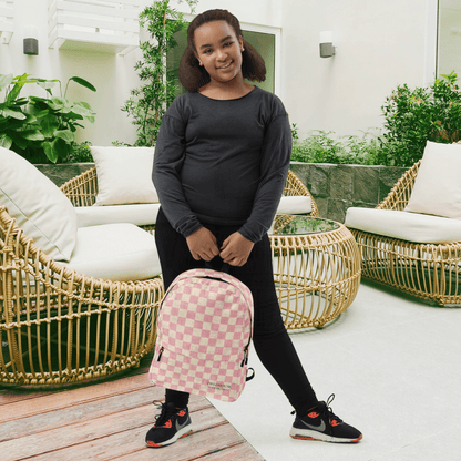 Person holding a pink checkered backpack in an outdoor setting with wicker furniture and plants.