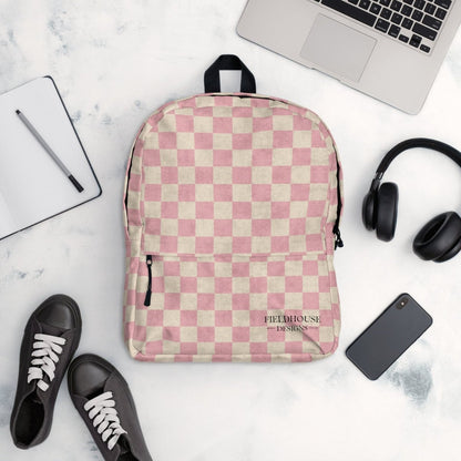 Pink and beige checkered backpack on a marble surface with a laptop, headphones, and shoes.