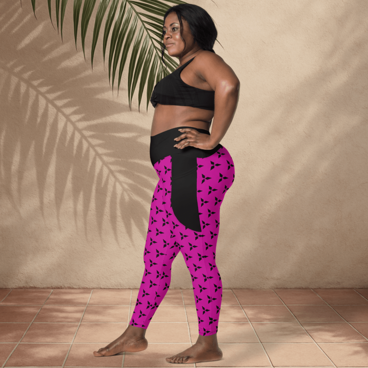 Woman wearing black sports bra and pink leggings with black patterns against a beige wall.