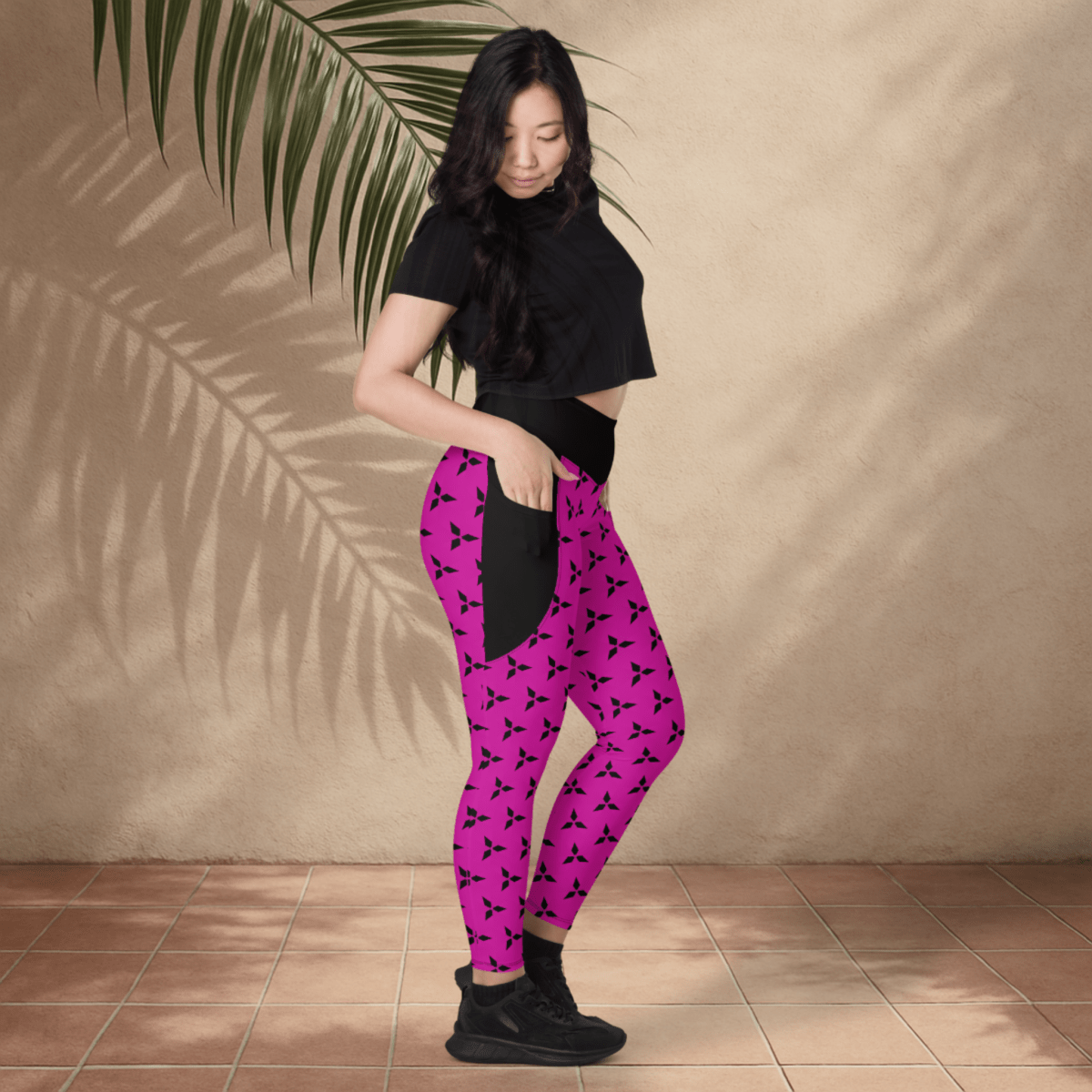 Person wearing black top and pink leggings with black patterns against a beige wall.
