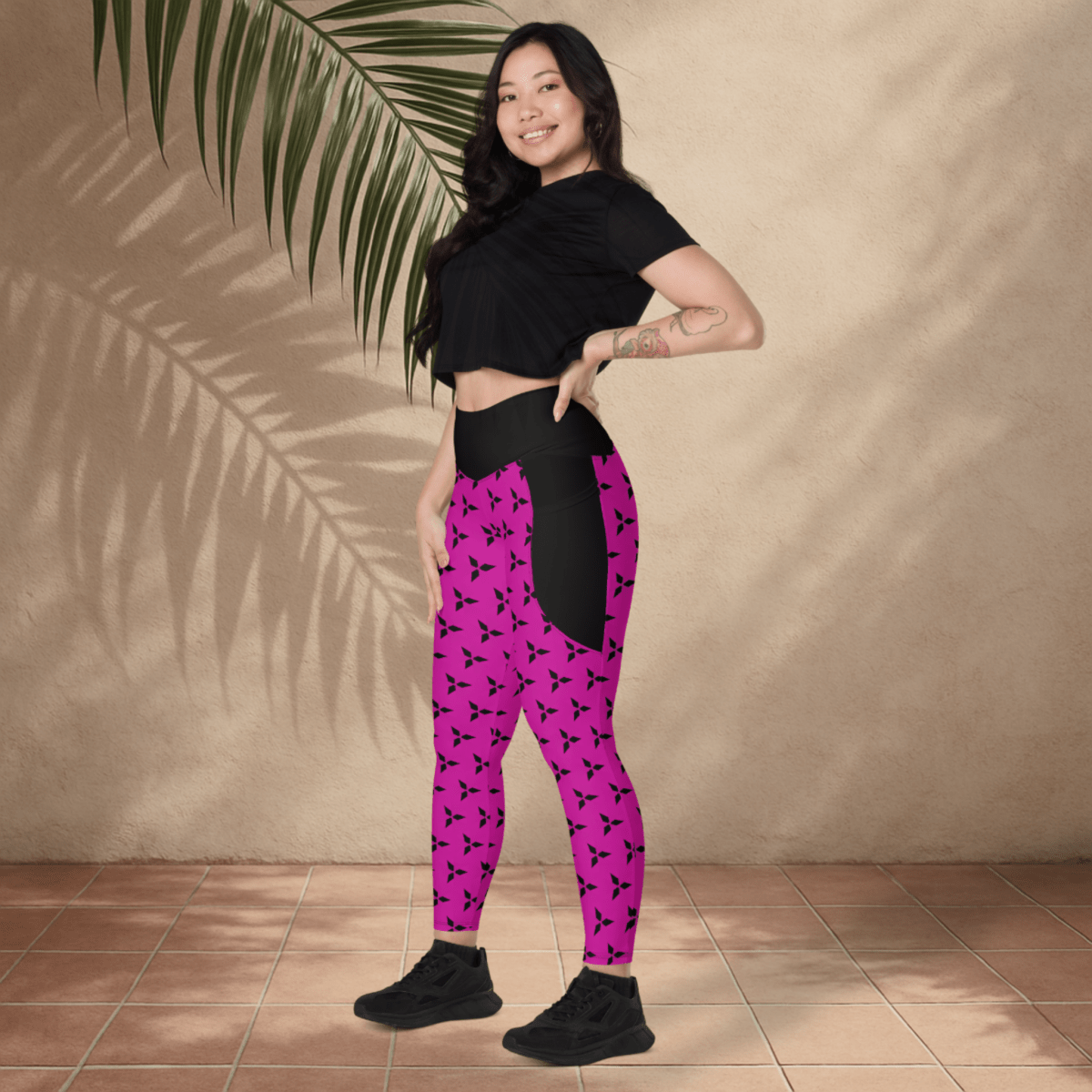 Woman wearing black top and pink leggings with black patterns against a beige wall.