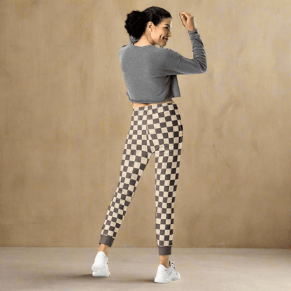 Woman wearing a gray long-sleeve top and checkered leggings against a beige wall.