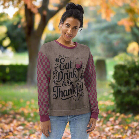 Woman wearing a sweater with 'Eat Drink & Be Thankful' text and wine glass design outdoors