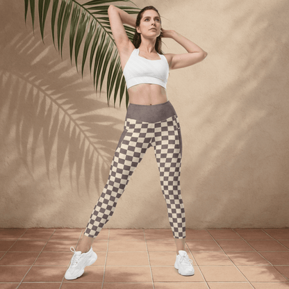 Woman wearing a white sports bra and checkered leggings standing against a beige wall with a palm leaf.