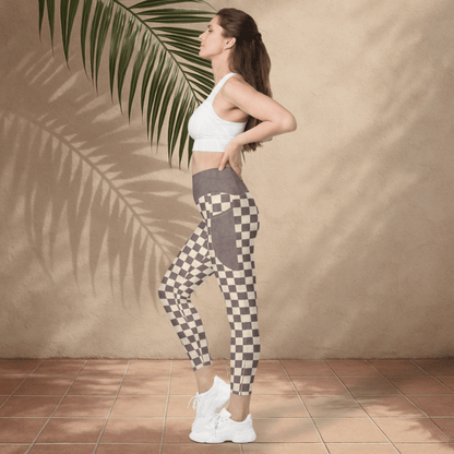 Woman wearing checkered leggings and a white sports bra against a beige wall with a palm leaf.