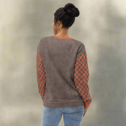Person wearing a brown sweatshirt with checkered sleeves against a neutral background