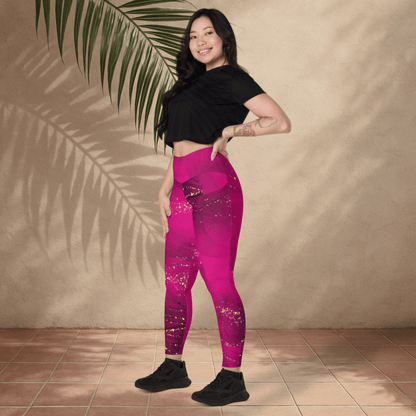 Woman wearing pink leggings and black top standing against a beige wall with a plant leaf.