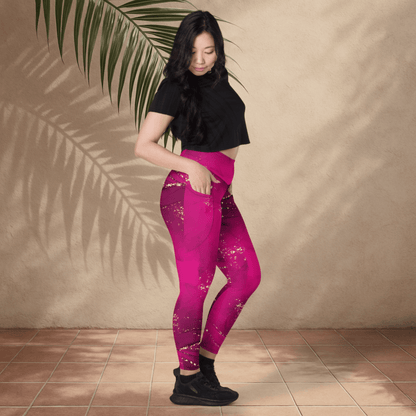Woman wearing a black crop top and pink leggings standing against a beige wall with a palm leaf.