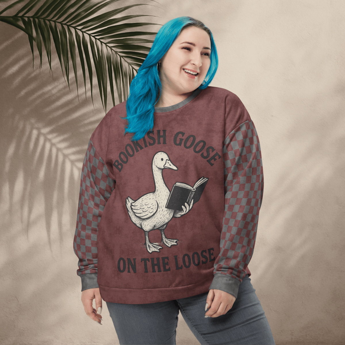 Person wearing a sweatshirt with a goose graphic and text, standing against a beige wall with a leafy branch.