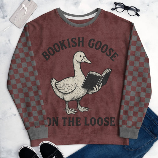 Burgundy crewneck sweatshirt with gray checkered sleeves. Featuring a goose reading a book graphic and text 'Bookish Goose on the Loose' on a marble surface