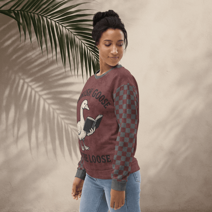 Woman wearing a burgundy crewneck sweater with a graphic design, standing against a beige wall with a palm leaf.