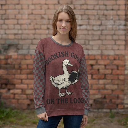 Person wearing a burgundy sweater with a goose graphic and text, standing against a brick wall.