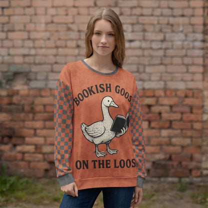 Person wearing a sweater with a goose reading a book and text 'Bookish Goose on the Loose"  in front of a brick wall