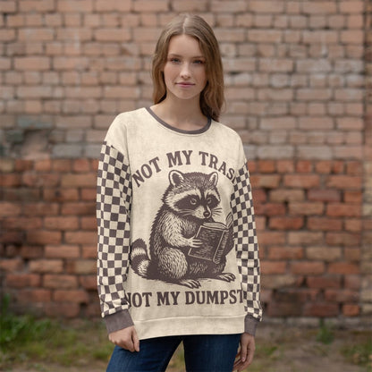 Woman wearing a sweater with a raccoon reading a book graphic and text "Not my Trash, Not my Dumpster" in front of a brick wall.
