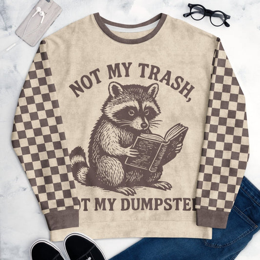 Beige crewneck sweatshirt with espresso checkered sleeves. Featuring a raccoon reading a book graphic and text 'Not my trash, not my dumpster' on a marble surface.