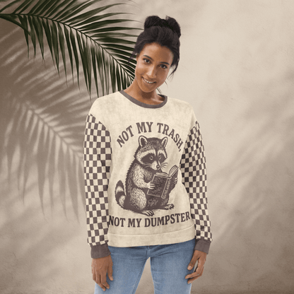 Beige crewneck sweatshirt with espresso checkered sleeves. Featuring a raccoon reading a book graphic and text 'Not my trash, not my dumpster' 