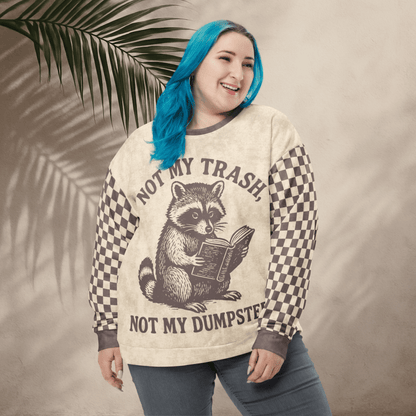 model wearing a Beige crewneck sweatshirt with espresso checkered sleeves. Featuring a raccoon reading a book graphic and text 'Not my trash, not my dumpster' 