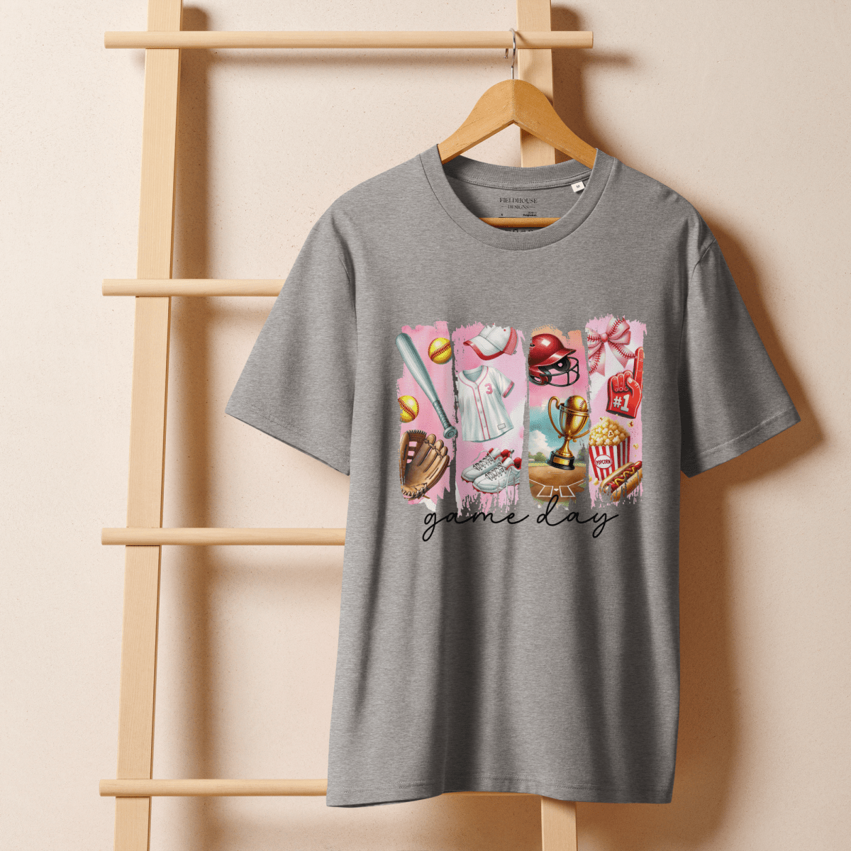 Gray t-shirt with "game day" graphic design on a wooden hanger against a beige wall.