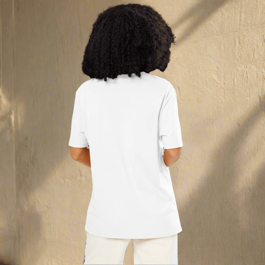 Person wearing a white t-shirt and pants standing against a beige wall.