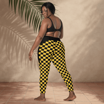 Person wearing black and yellow checkered pants standing against a beige wall.