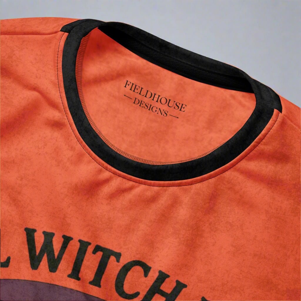 Close-up of an orange shirt with black text and neckline, featuring 'Fieldhouse Designs'.