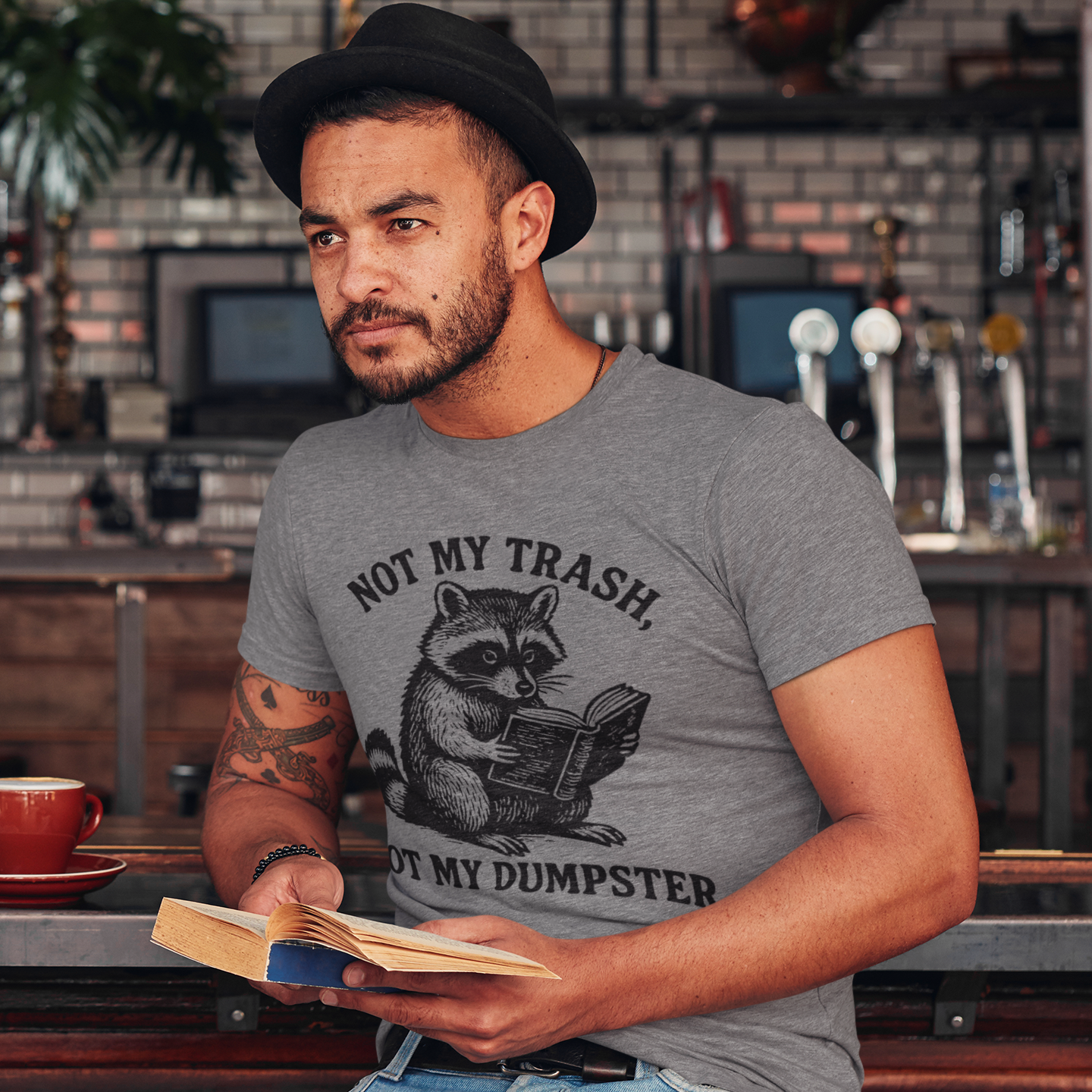 Man wearing a t-shirt with a raccoon graphic and text, sitting in a bar.