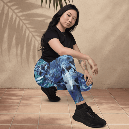 Woman wearing black t-shirt and blue tie dye pattern leggings sitting on a tiled floor with a beige wall and plant leaf in the background.