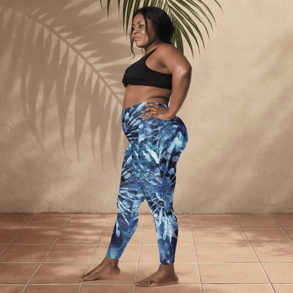 Woman wearing blue tie-dye leggings and black sports bra standing against a beige wall.