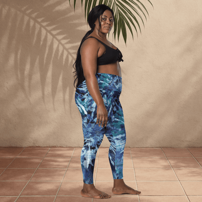 Woman wearing blue tie-dye leggings and black top standing against a beige wall.